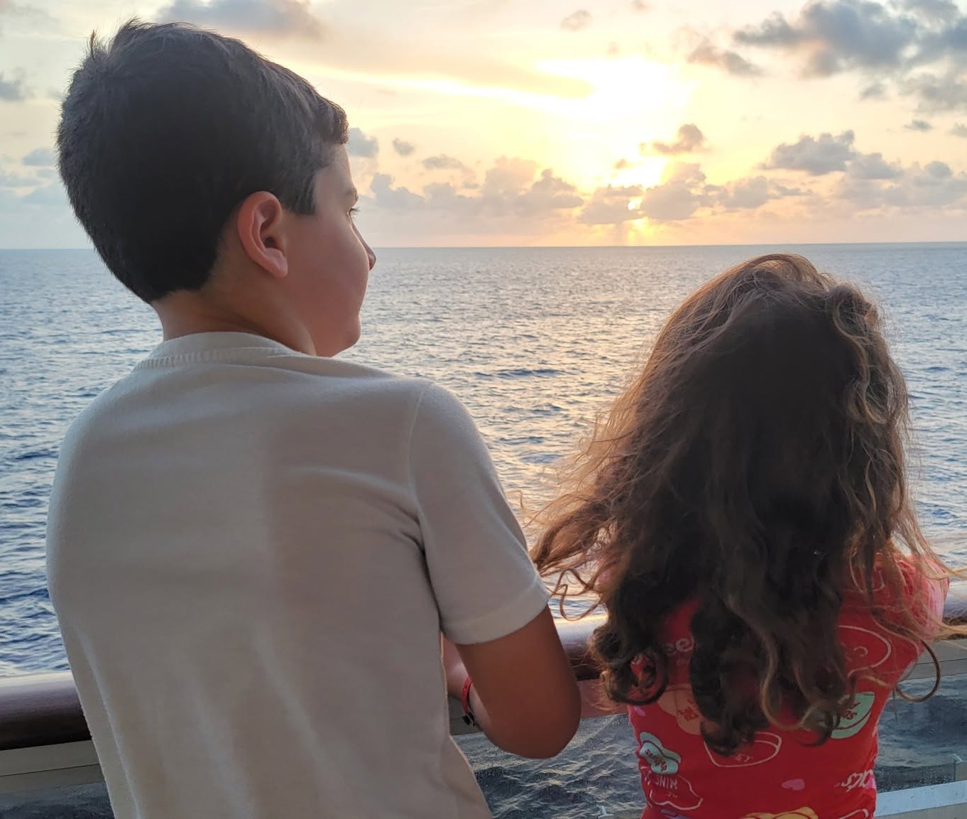 Siblings watching the sunset from a cruise ship deck